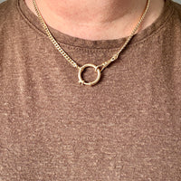 A close-up of a person wearing an 18k gold watch chain necklace paired with a brown knit top.