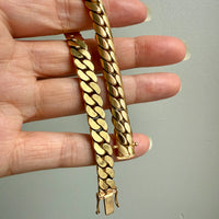 Gold chain bracelet held by a hand against a plain background