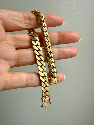 Gold chain bracelet held by a hand against a plain background