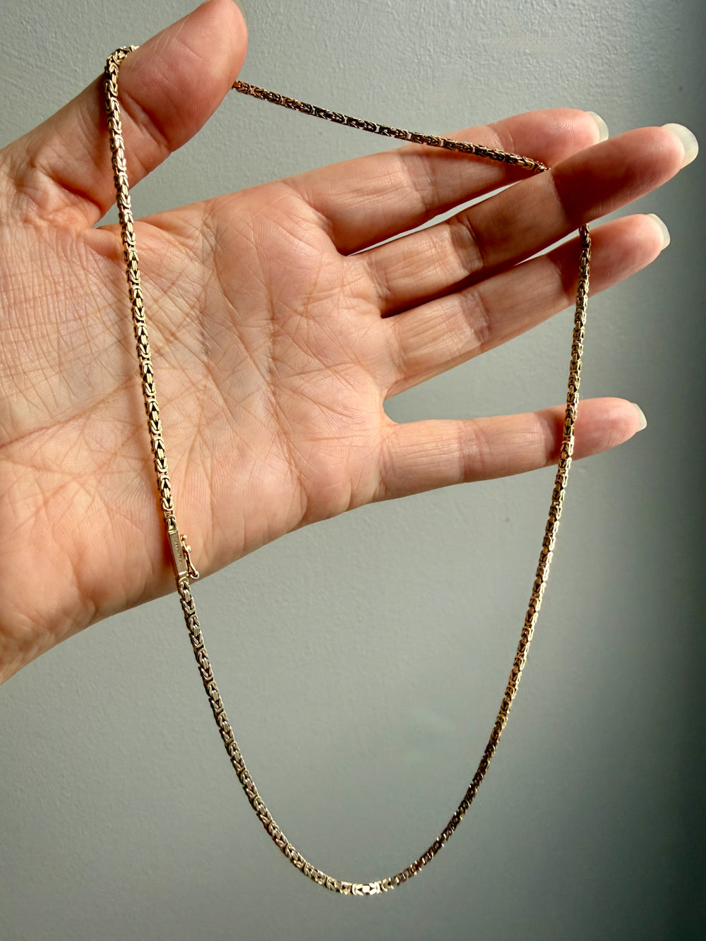 Gold chain held by a hand against a neutral background