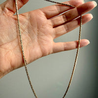 Gold chain held by a hand against a neutral background