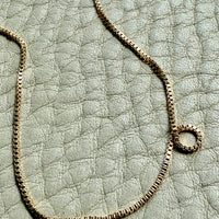 18k Gold box chain necklace on a textured light gray surface
