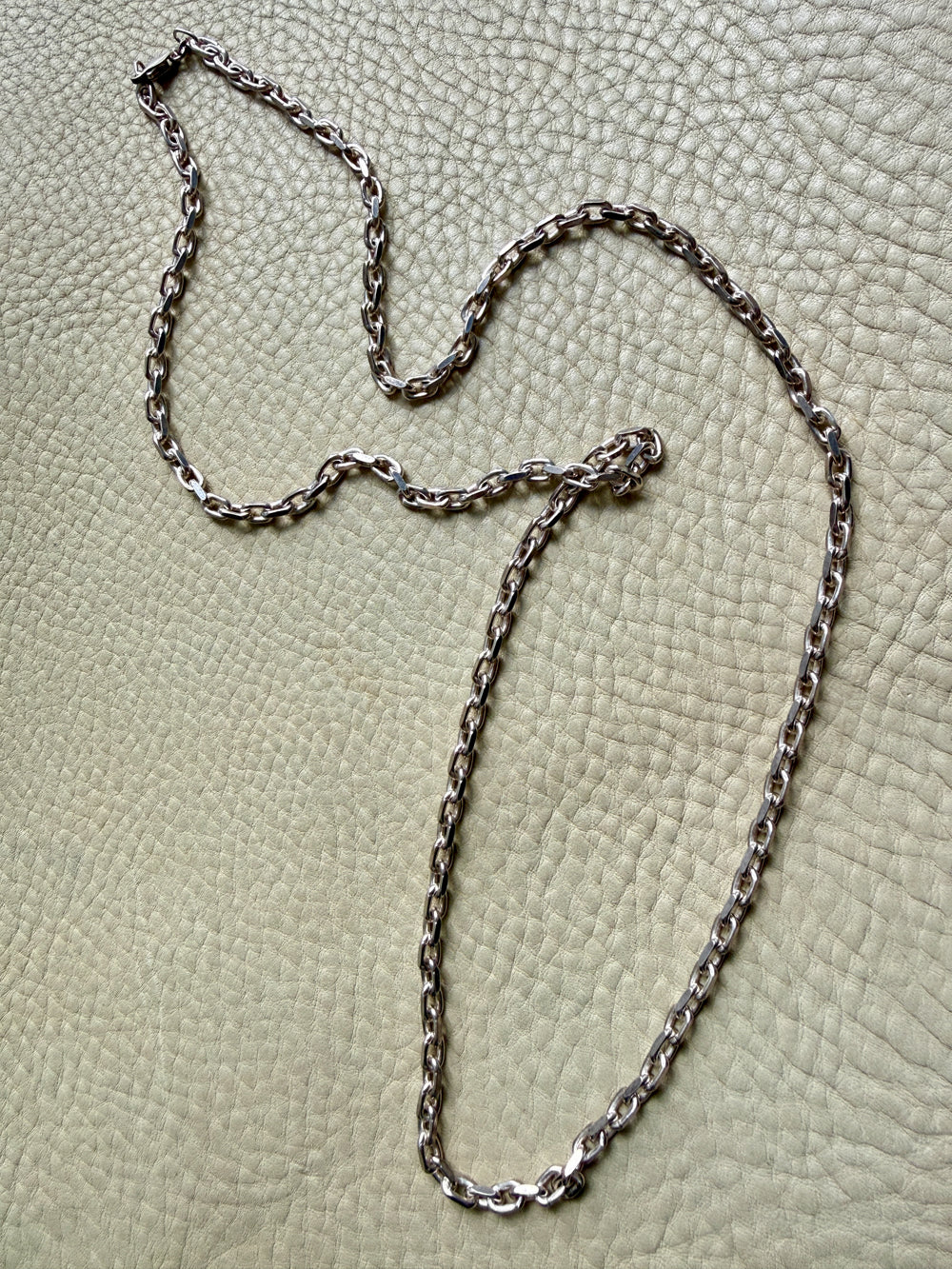 Silver chain necklace on a textured beige surface