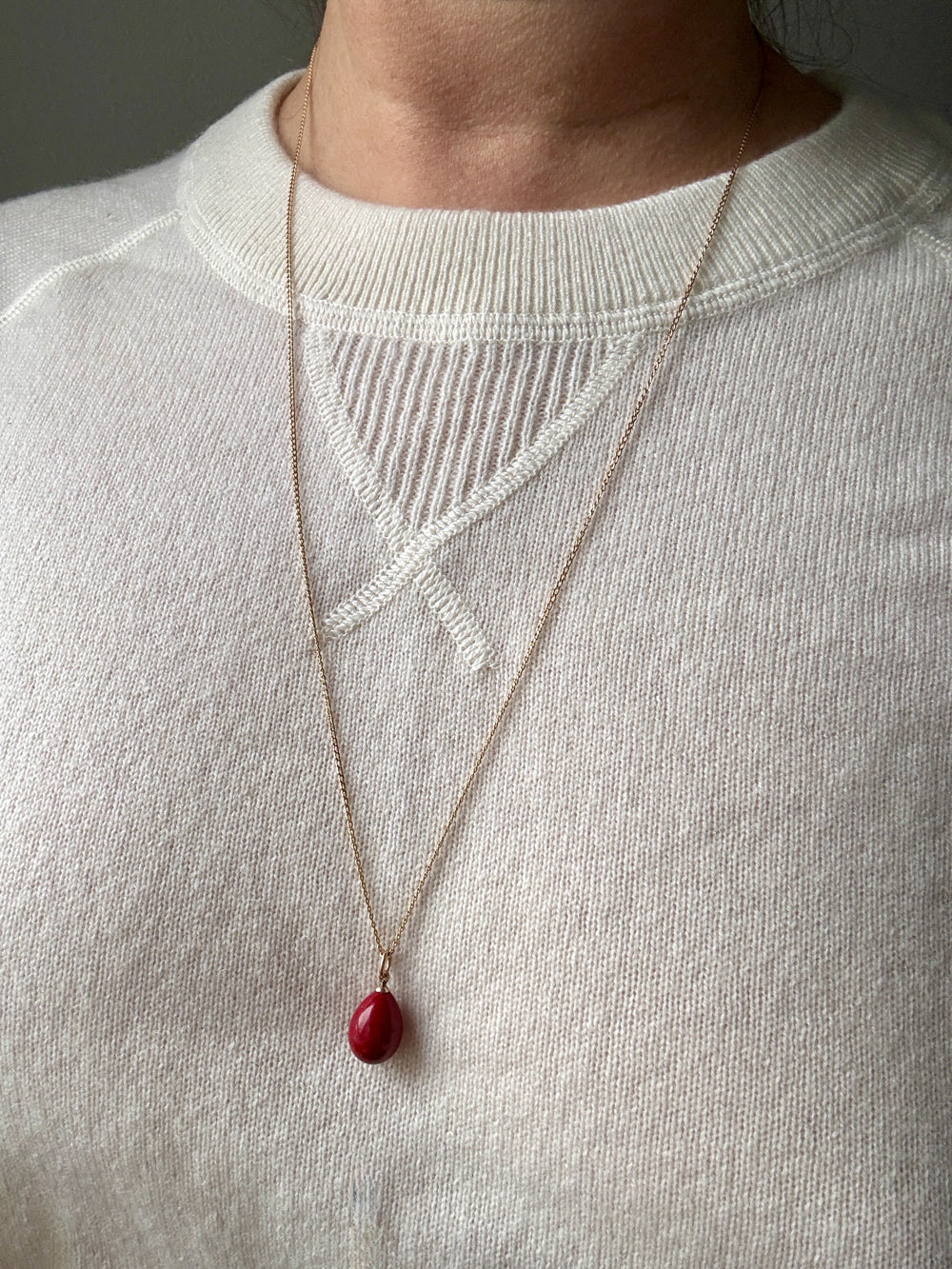 Necklace with a red pendant worn by a person on a plain background