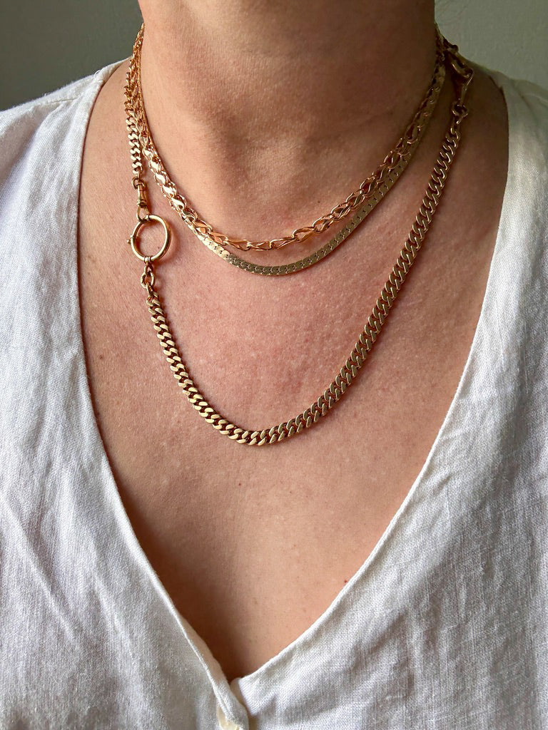 Close-up of a person wearing gold chain necklaces on a plain background PenelopePenelope.com