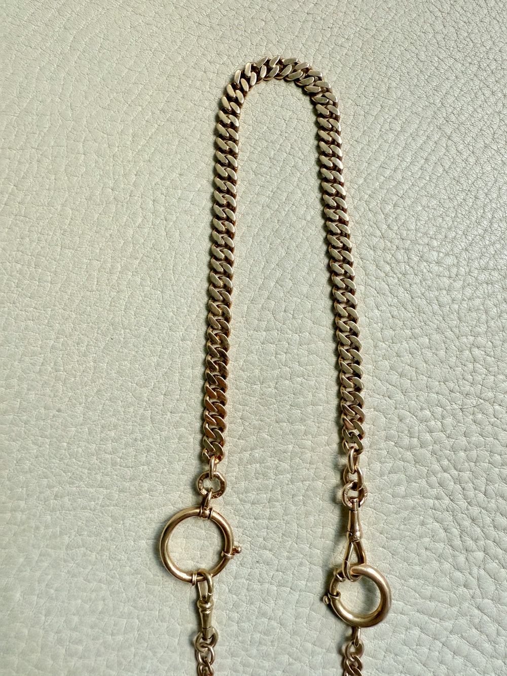 Gold chain with bolt clasps on a textured light gray background