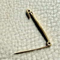 18k gold vintage safety pin brooch on a textured light gray background