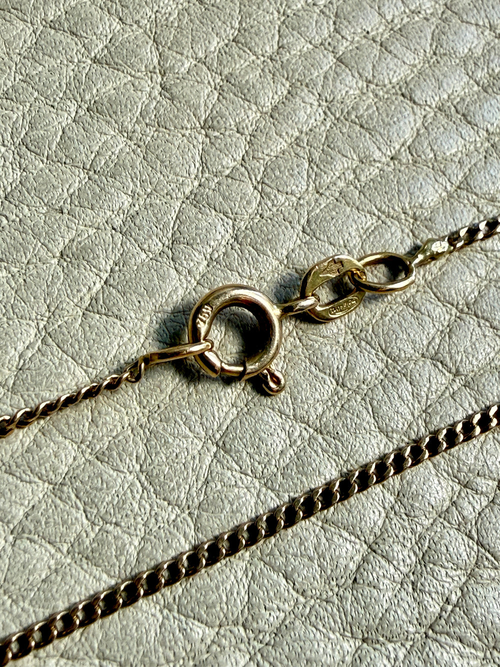 Close-up of a gold necklace clasp on a textured light gray background