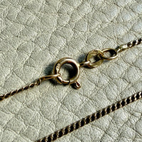 Close-up of a gold necklace clasp on a textured light gray background