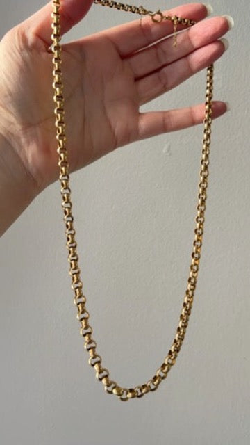 Gold chain held by a hand against a plain background