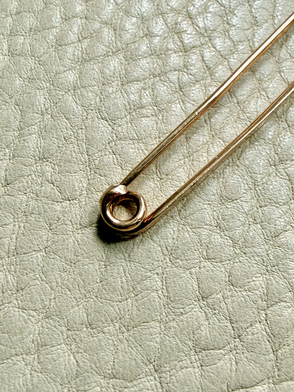 Gold safety pin on a textured light gray background