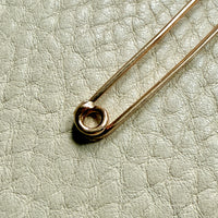 Gold safety pin on a textured light gray background