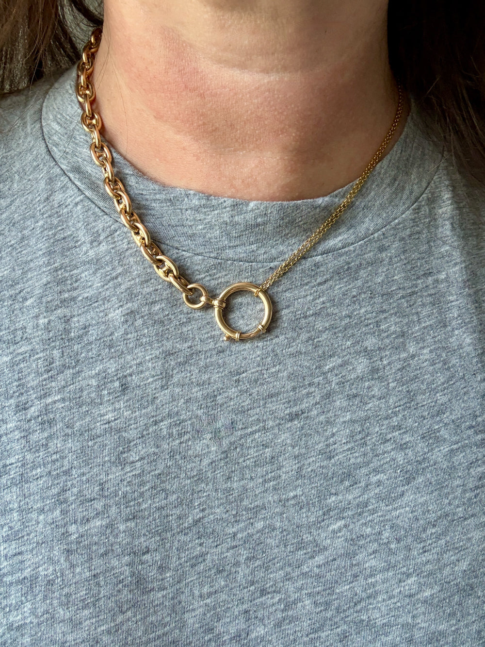Gold necklace with a circular pendant worn by a person on a gray shirt