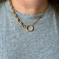 Gold necklace with a circular pendant worn by a person on a gray shirt
