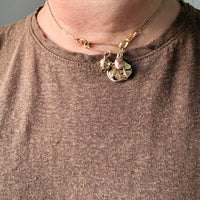 Close-up of a person wearing a gold necklace with charms on a plain background