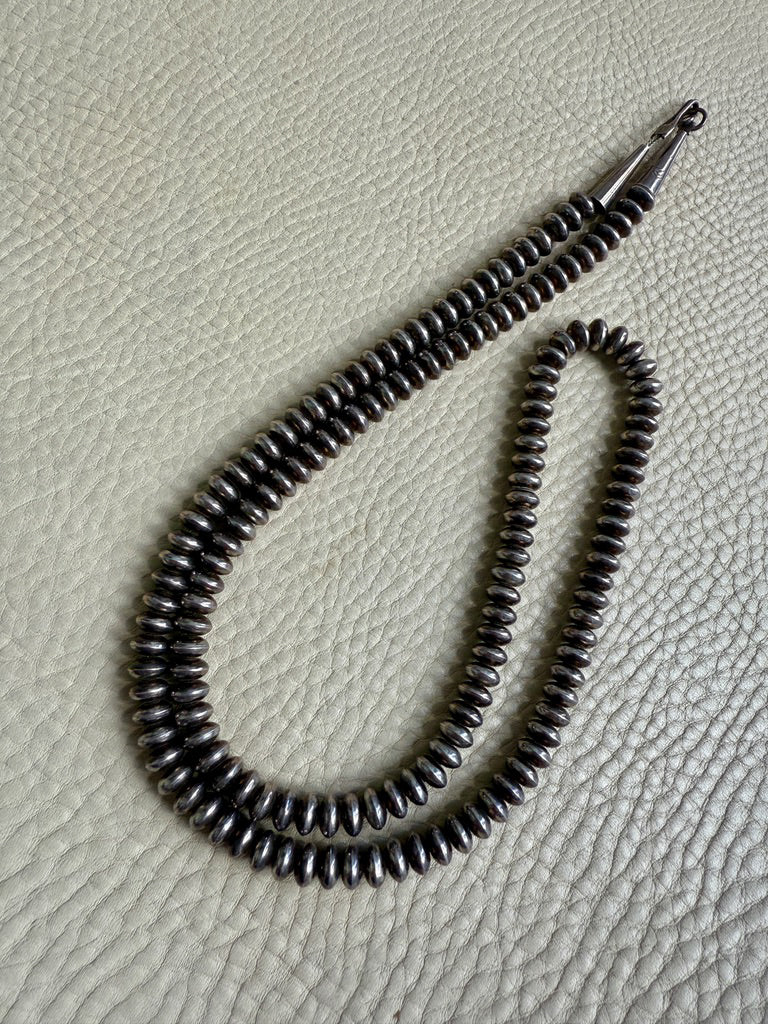 Silver beaded necklace on a textured beige surface