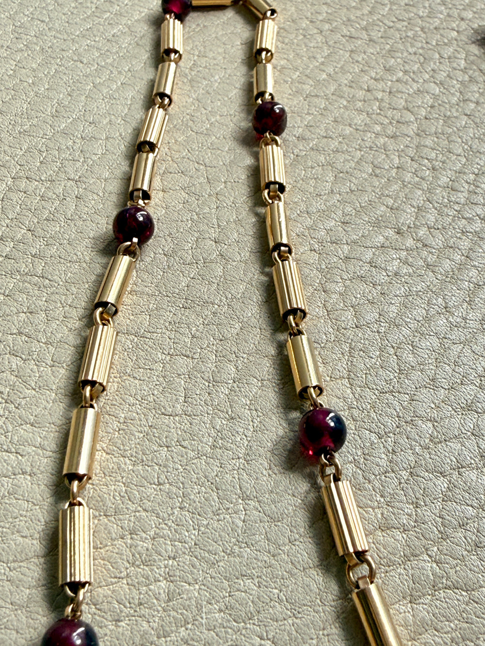 Gold necklace with red beads on a light gray textured background