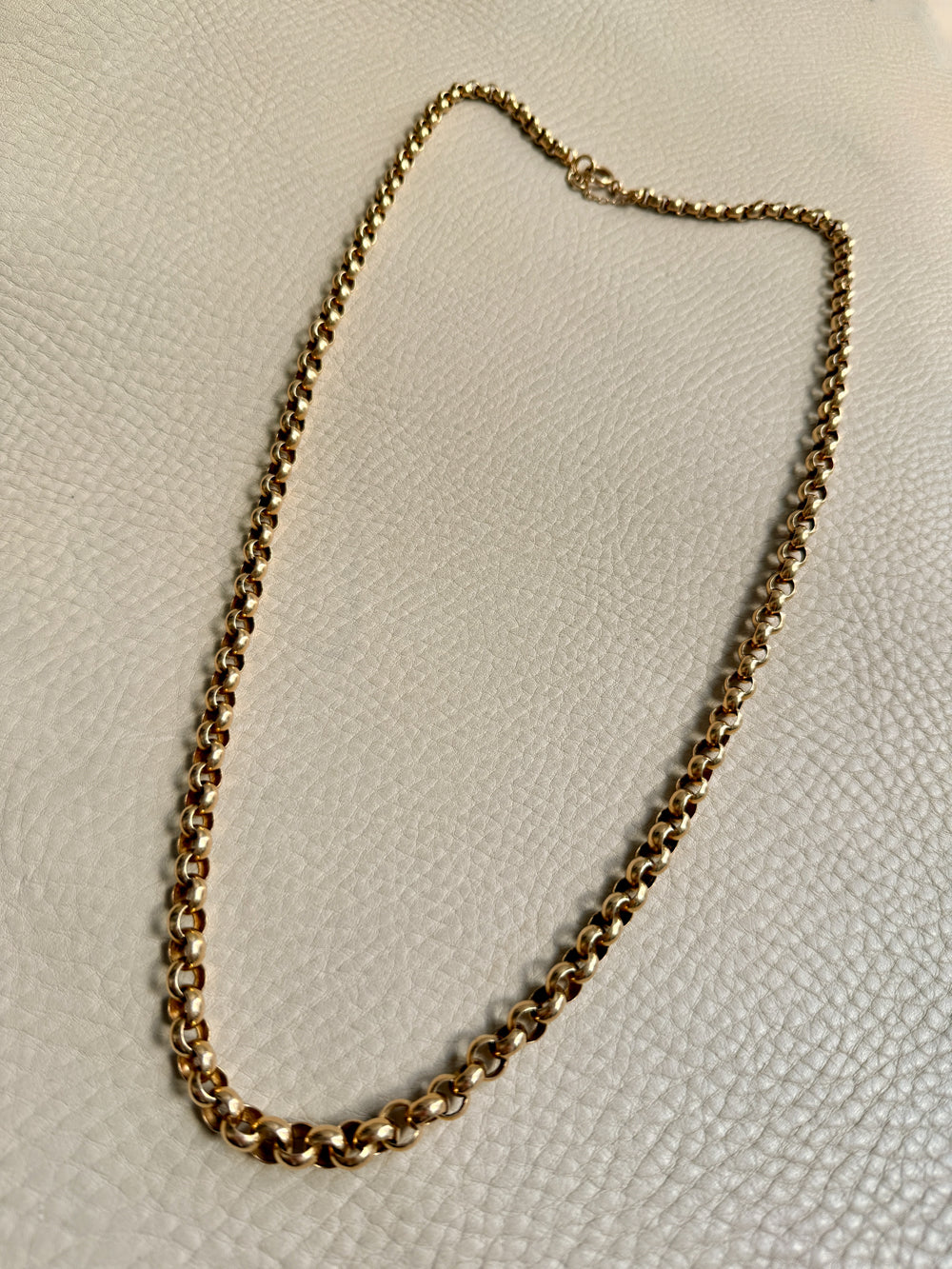 Gold chain necklace on a light beige textured surface