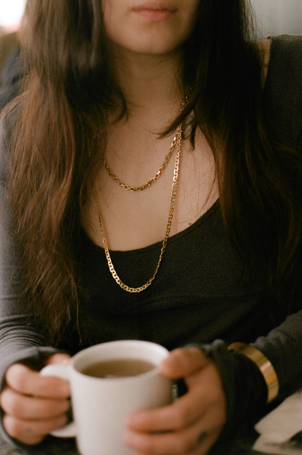 Person holding a white mug wearing gold chains with a blurred background