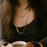 Person holding a white mug wearing gold chains with a blurred background