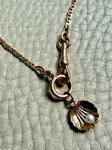 Necklace with a shell and pearl charm on a textured surface