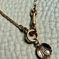 Necklace with a shell and pearl charm on a textured surface