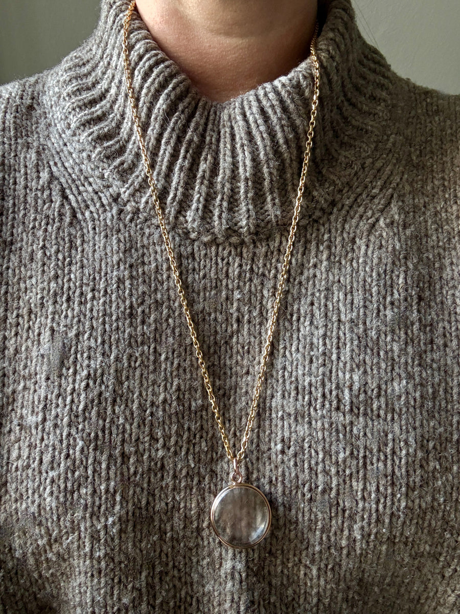 Necklace with a pendant worn on a person wearing a gray knit sweater.