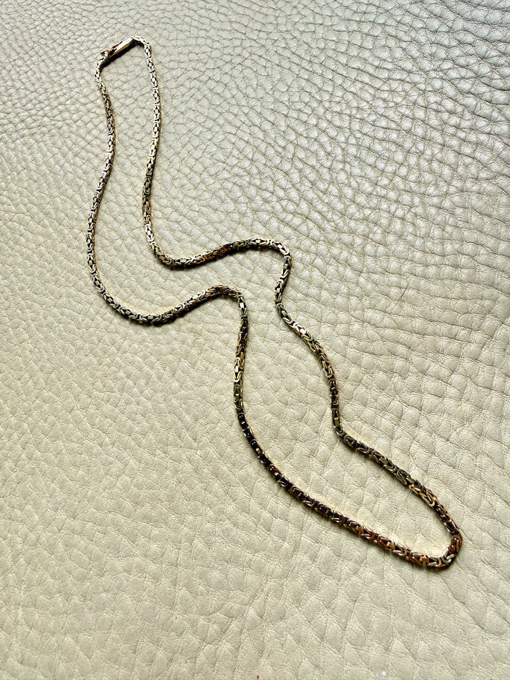 14k gold Gold byzantine chain necklace on a textured beige surface penelopepenelope.com fine jewelry