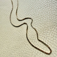 14k gold Gold byzantine chain necklace on a textured beige surface penelopepenelope.com fine jewelry