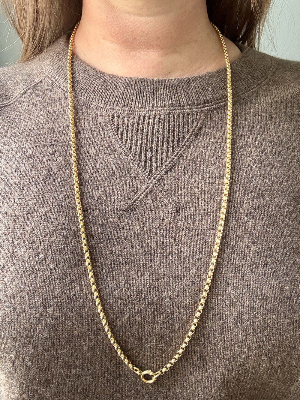 Gold chain necklace on a person wearing a brown sweater