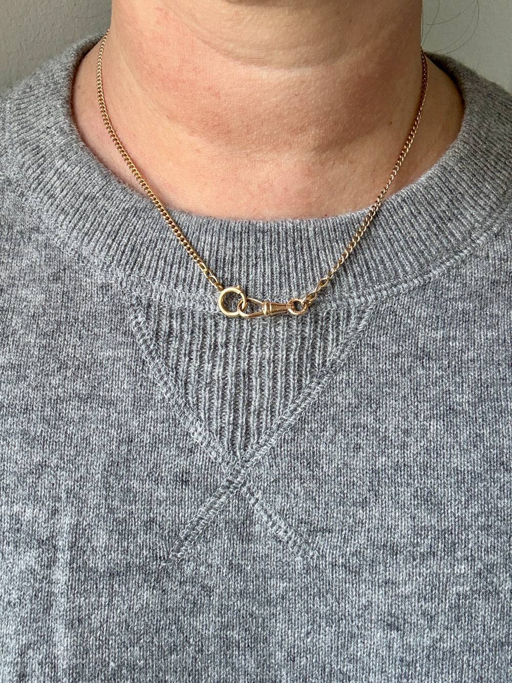 Gold necklace worn by a person in a gray sweater
