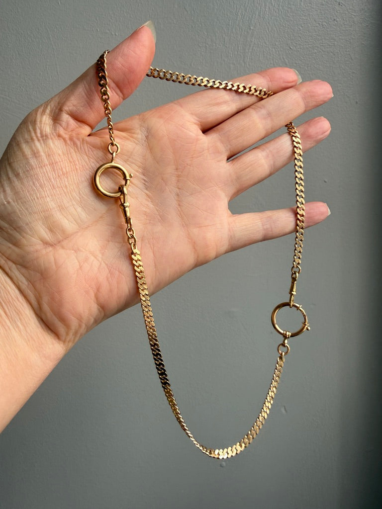 18k Gold vintage watch chain necklace held by a hand against a gray background