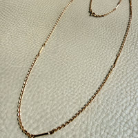 Gold chain necklace on a textured beige surface