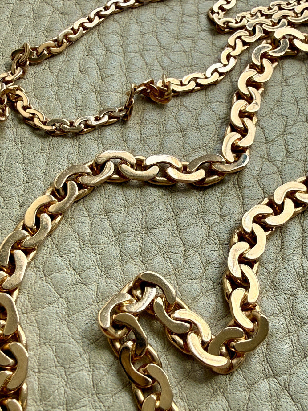 Gold chain necklaces on a textured green surface