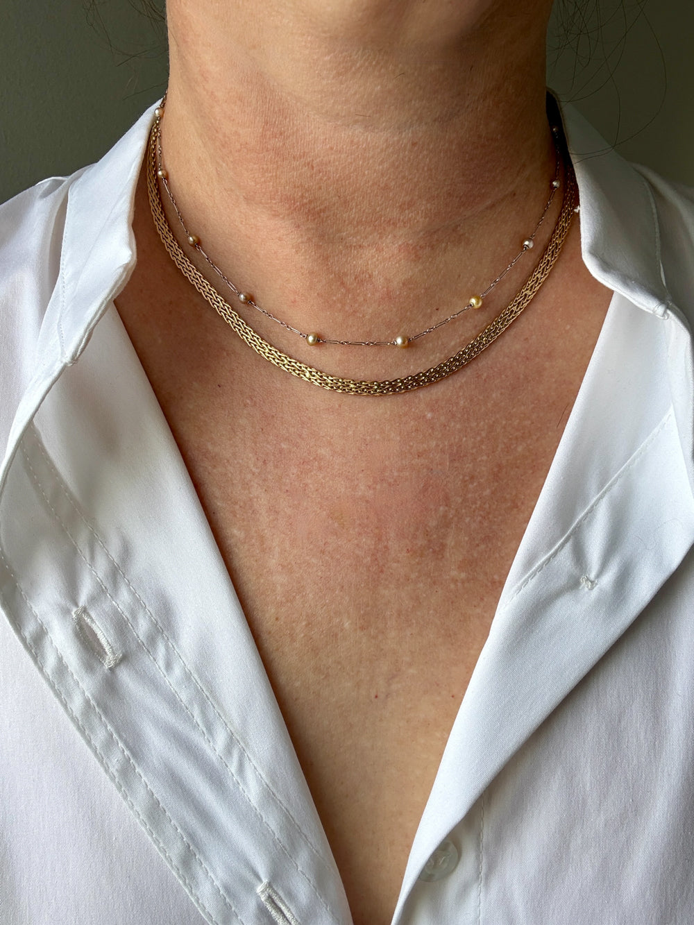 Close-up of a person wearing a white shirt with gold necklaces.