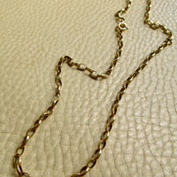 An 9k gold chain necklace with a twisted oval link design, laid out on a textured beige leather surface.