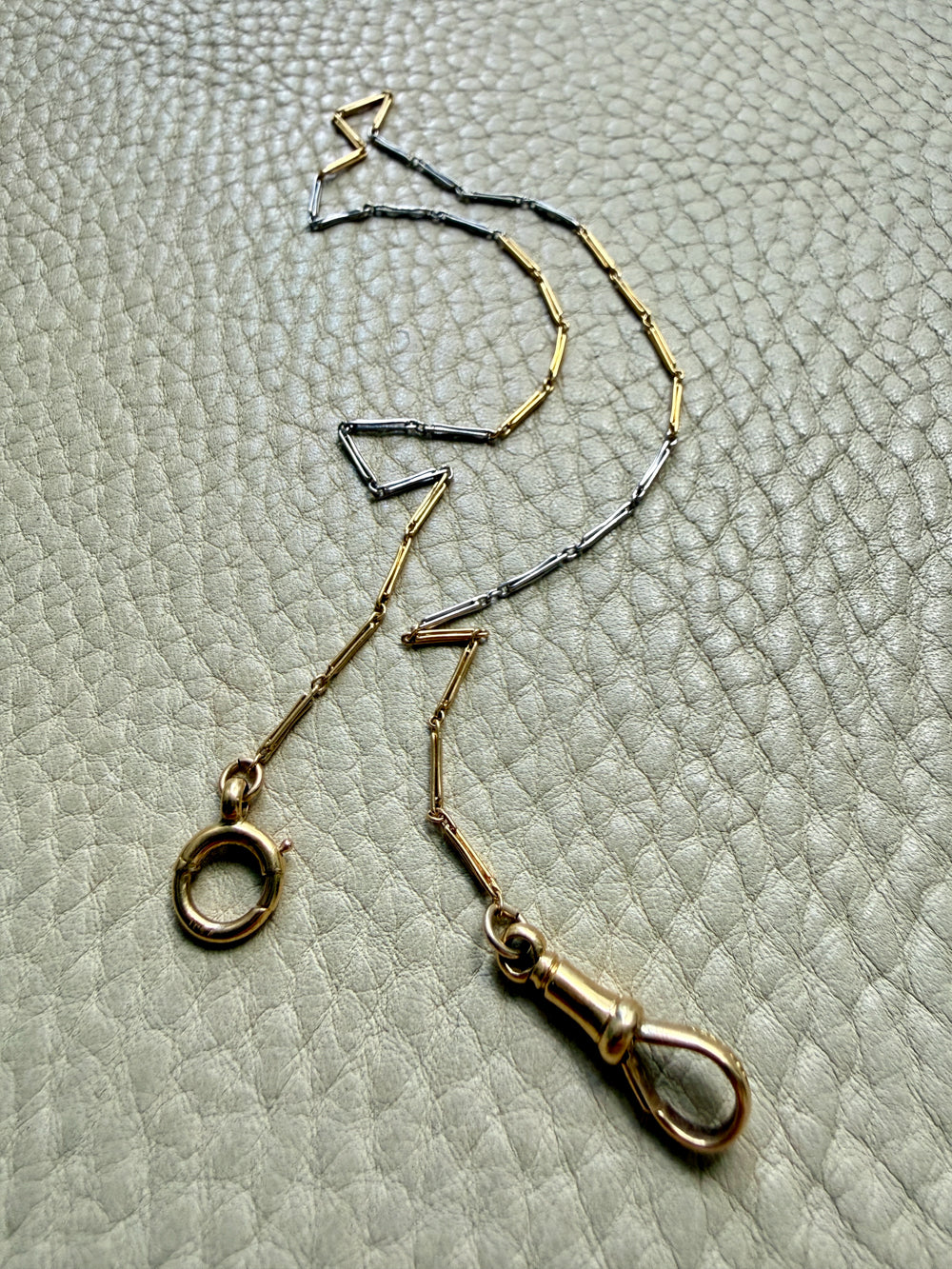 18k Gold and platinum watch chain with clip on a textured beige background