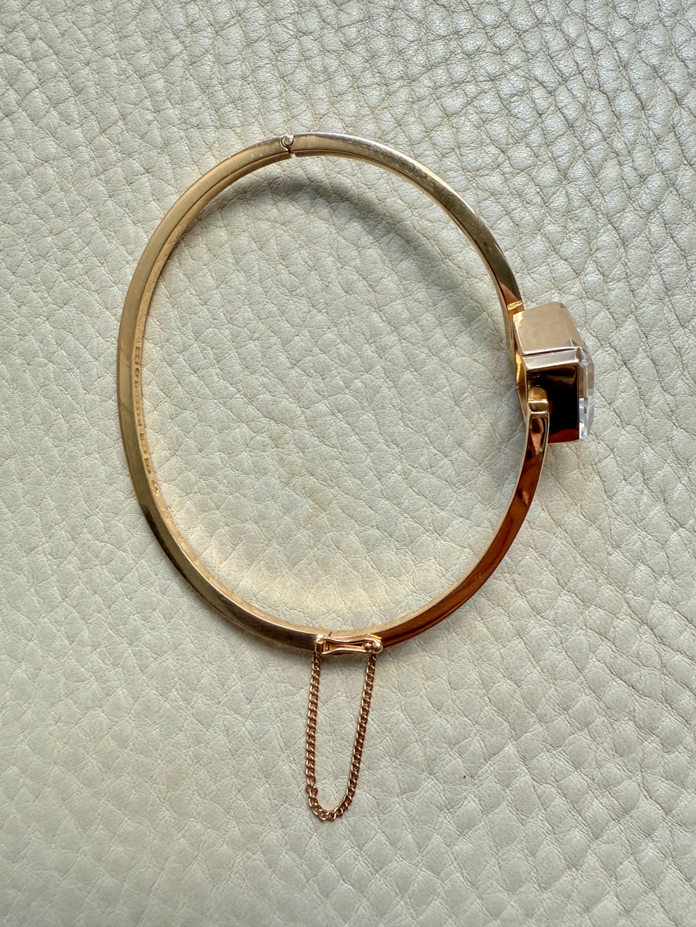 Gold bracelet with a chain on a textured light green surface