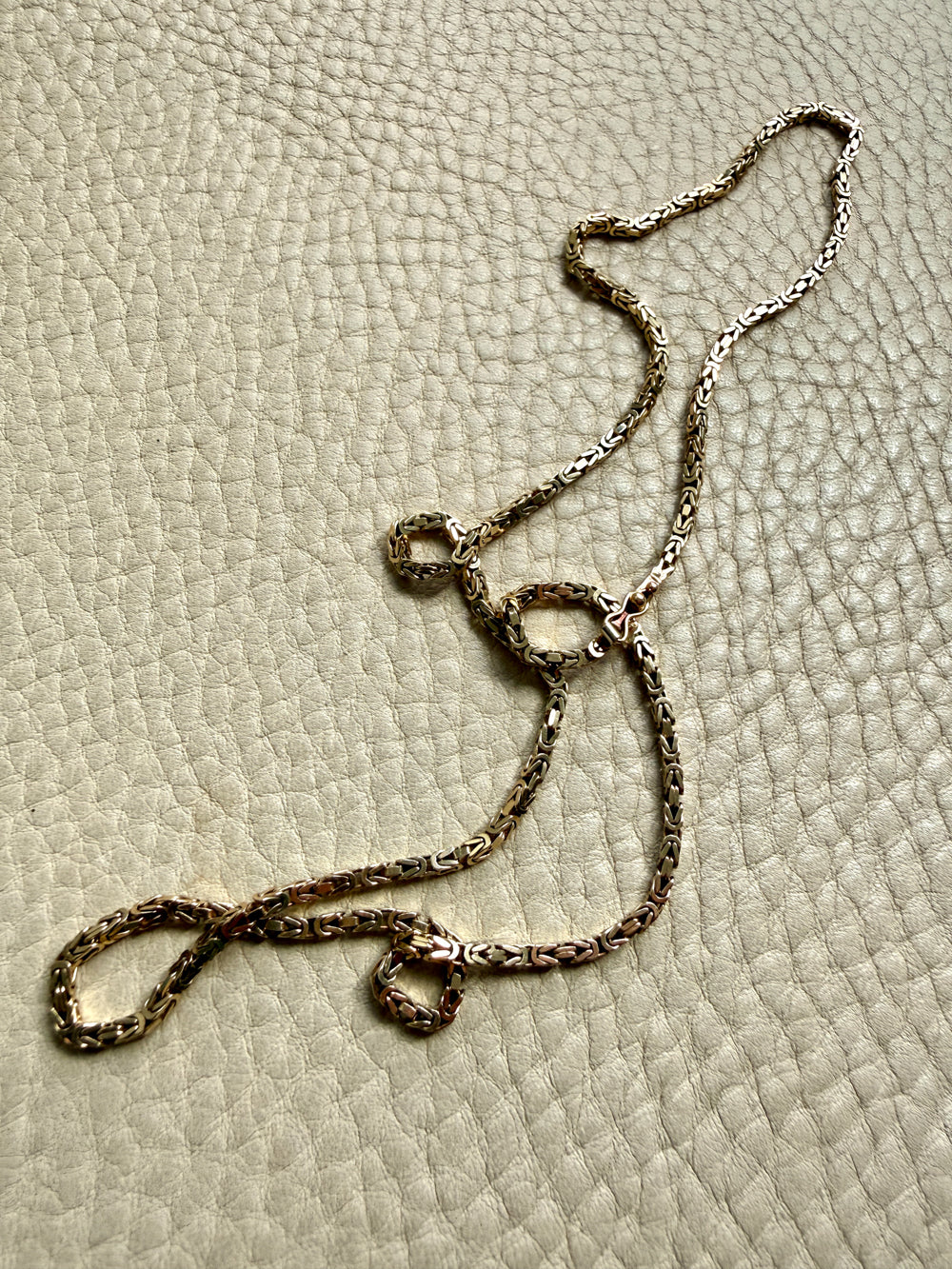 14k gold Gold byzantine chain necklace on a textured beige surface penelopepenelope.com fine jewelry