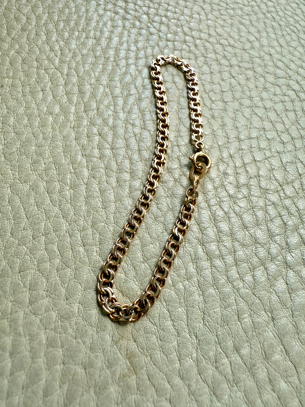 Gold chain bracelet on a light green textured surface