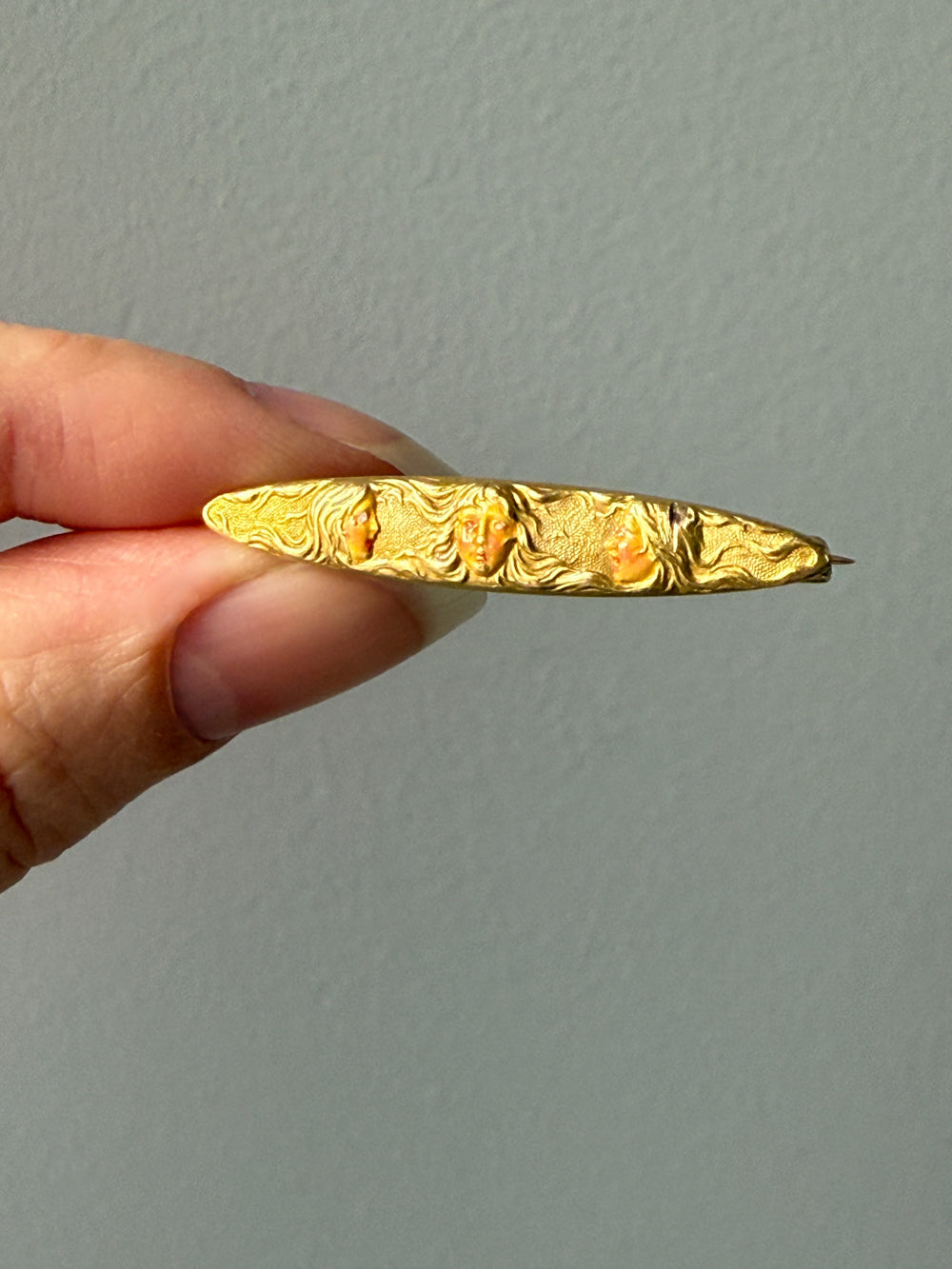 14k Gold enamel brooch with intricate design held by a hand against a plain background