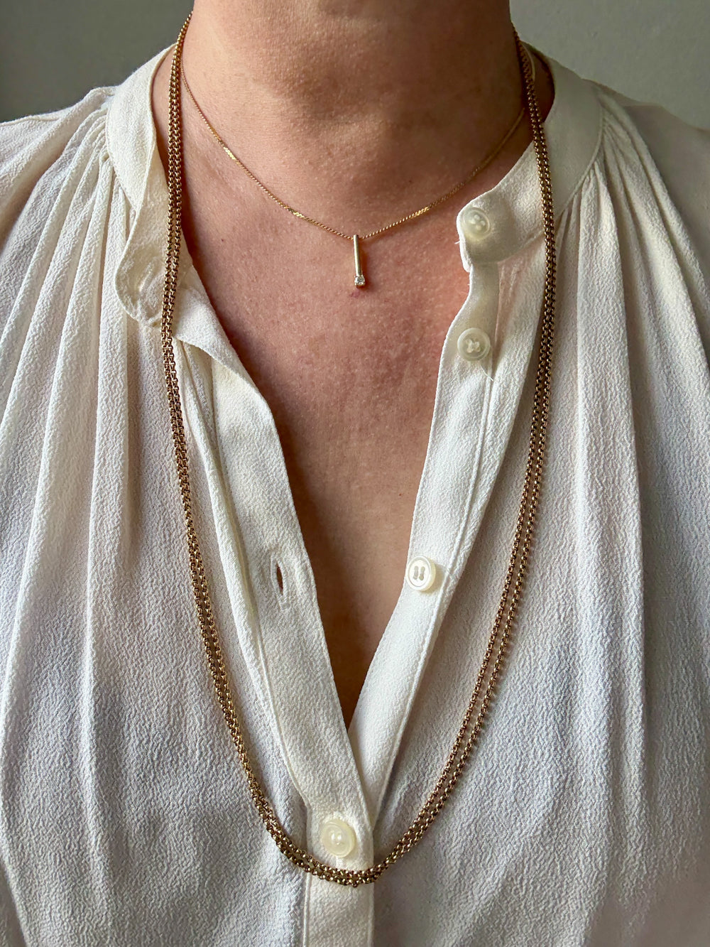 Person wearing a long gold necklace with a white shirt.