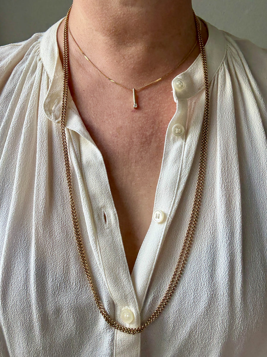 Person wearing a long gold necklace with a white shirt.