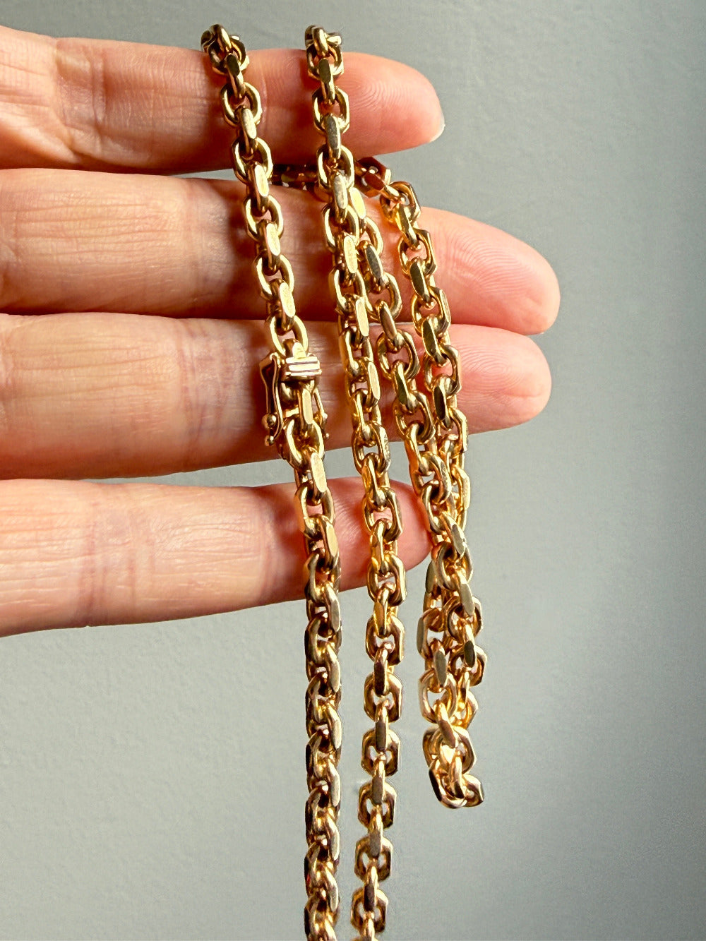 vintage 18k Gold biker chain held by a hand against a gray background