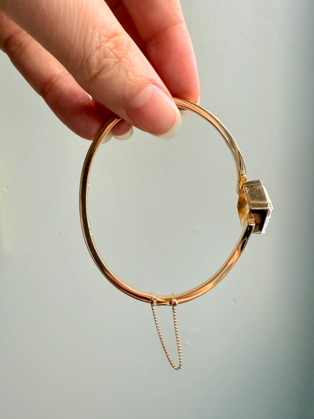 Gold bracelet with a clasp held by a hand against a light background