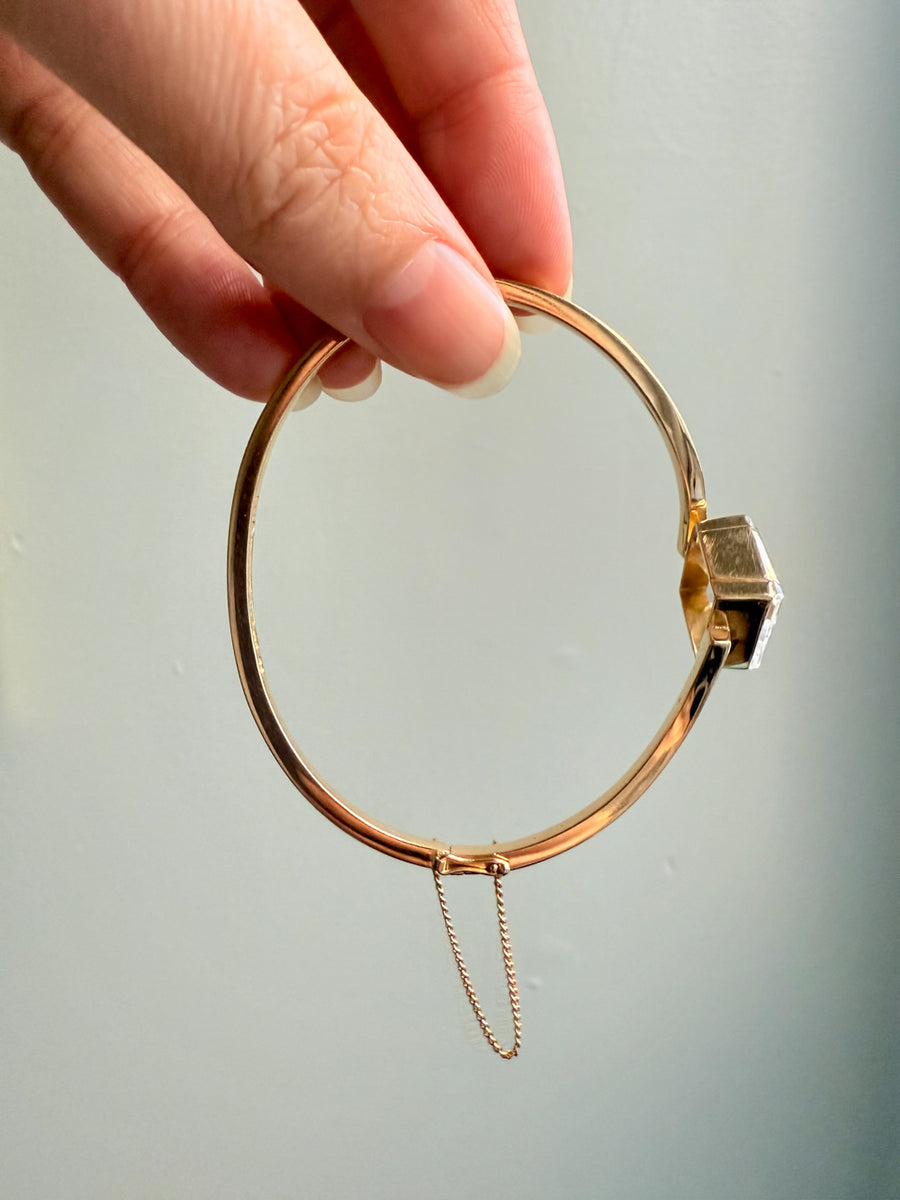 Gold bracelet with a clasp held by a hand against a light background
