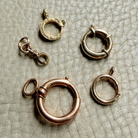 Set of gold bolt clasp jewelry components on a textured beige surface