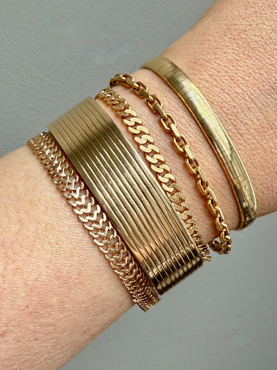 Gold bracelets on a wrist against a gray background