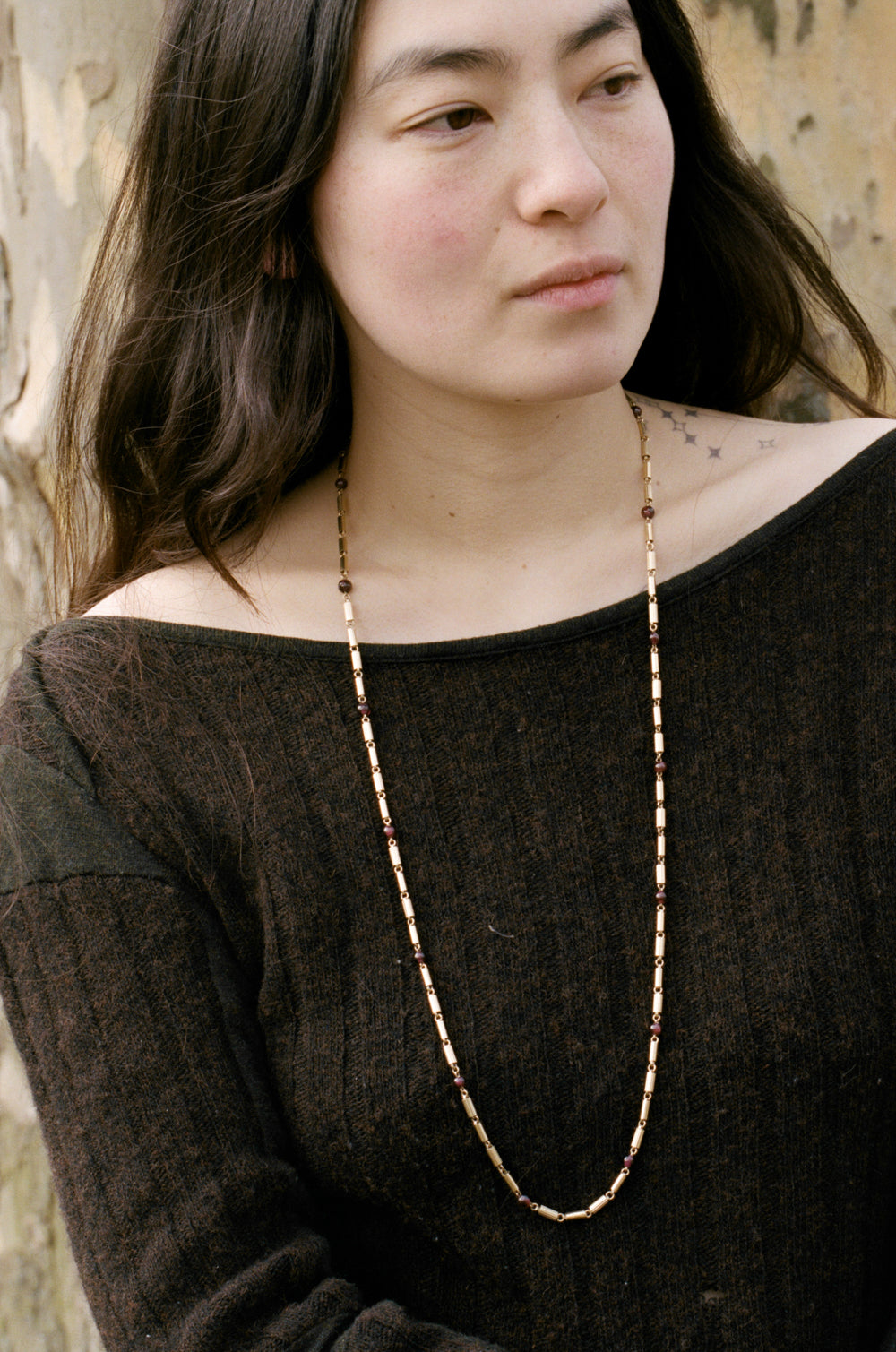Woman wearing a vintage long 18k gold and garnet necklace against a neutral background penelopepenelope.com