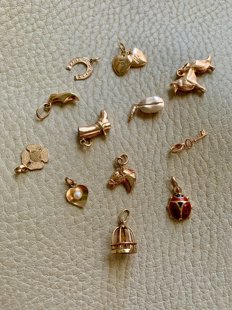 a collection of vintage swedish 18k gold charms or pendants. Included are a collie, a birdcage, a key, a coffee bean, a horseshoe, a moroccan slipper, a heart, a ladybug